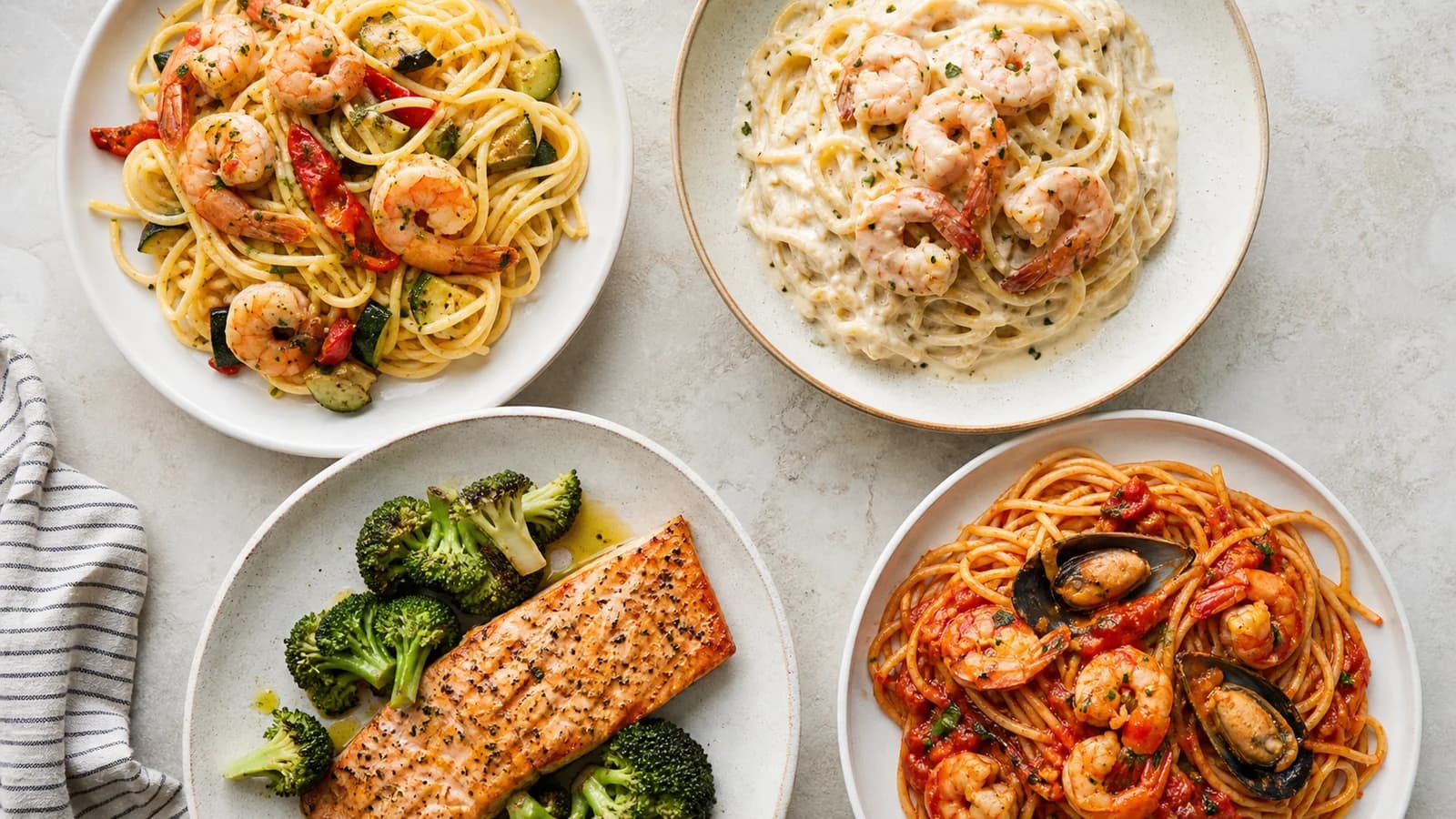 An original overhead comparison of shrimp pasta, creamy seafood pasta and grilled salmon